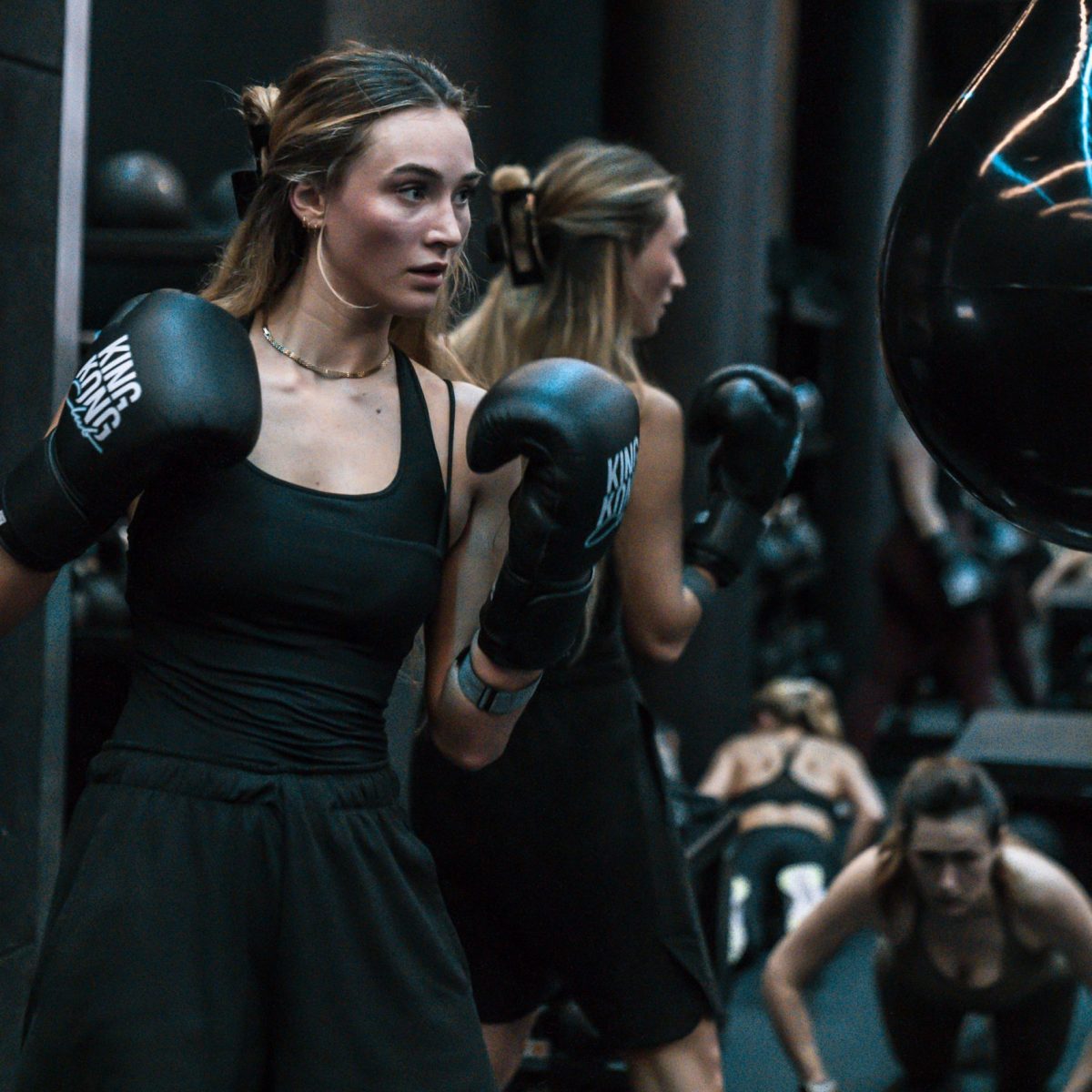 Junge Frau die vor dem Boxsack steht mit Boxhandschuhen.
