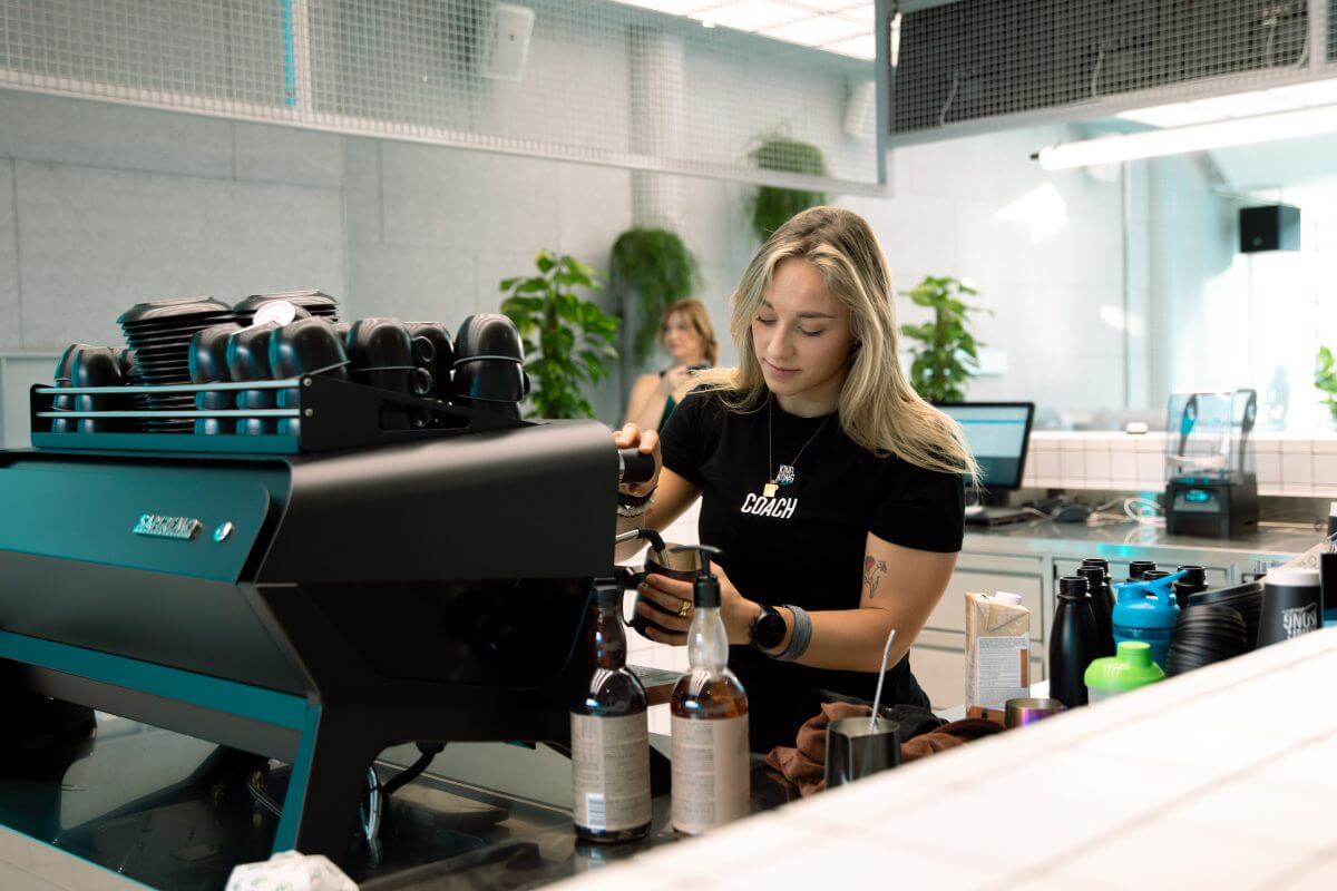 Personal Group Trainerin macht sich Kaffee an der Wet Bar im King Kong Club Salzburg.