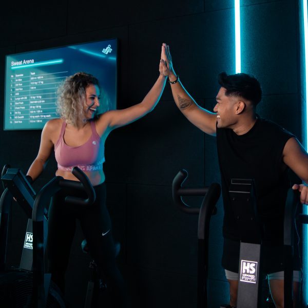 Junge Frau und junger Mann an Indoor-Fahrrädern schlagen mit den Händen ein